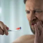 A man feeling the pain of gum disease. Learn more about gum disease. What is it? How to precent it.